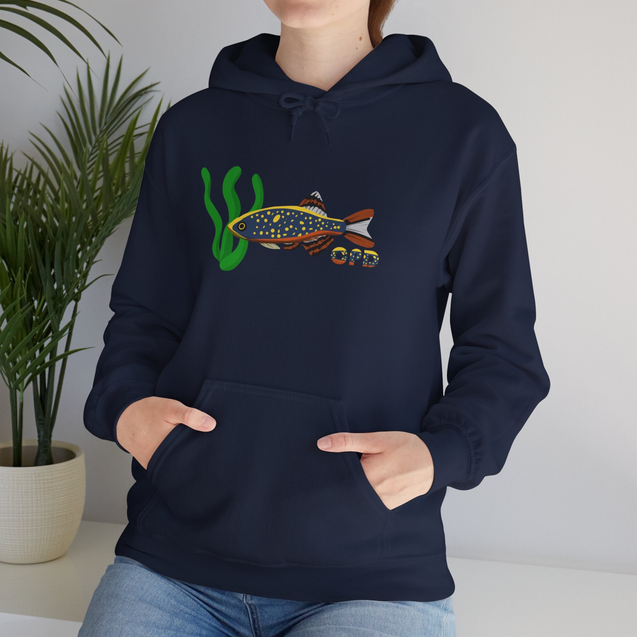 Woman in blue hoodie with Celestial Pearl Danio fish print, sitting by plant