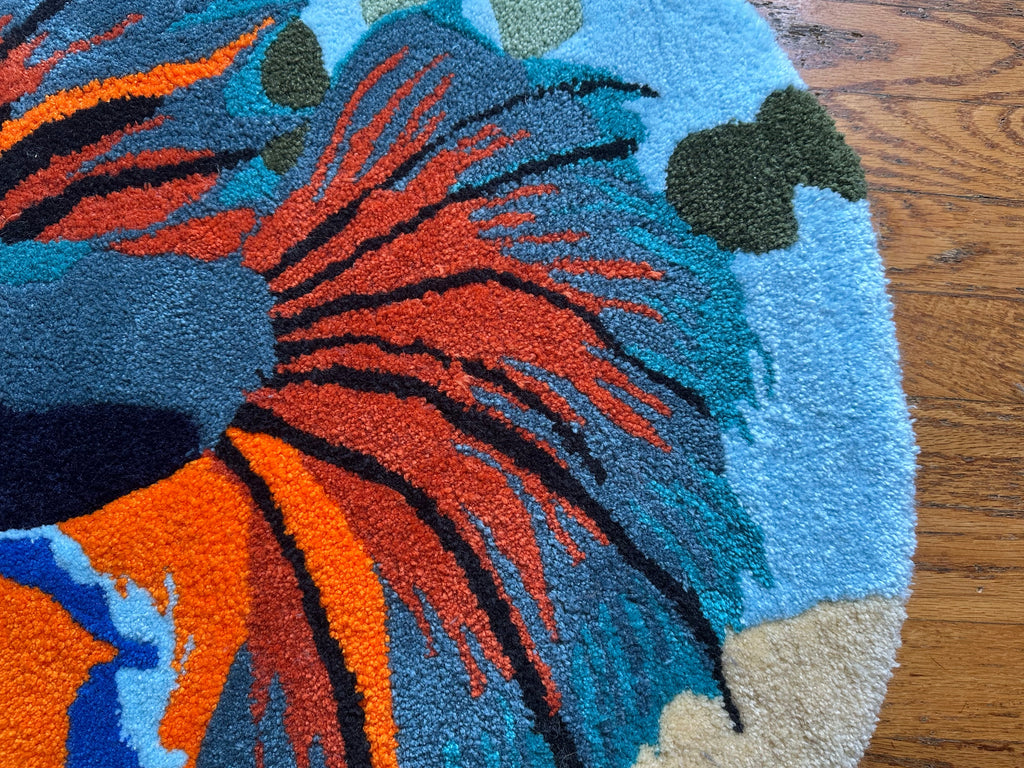 Close-up of colorful handmade betta fish rug with orange, blue, and green details on wood floor