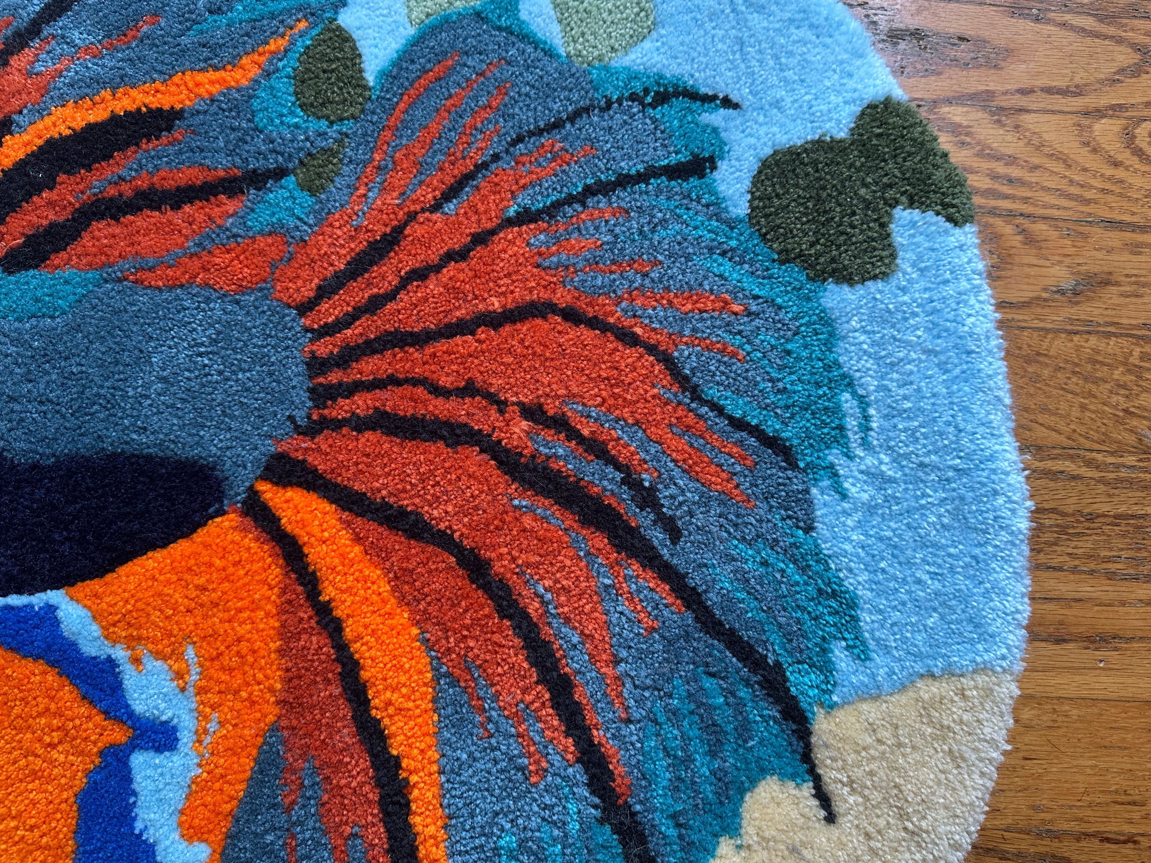 Close-up of colorful handmade betta fish rug with orange, blue, and green details on wood floor