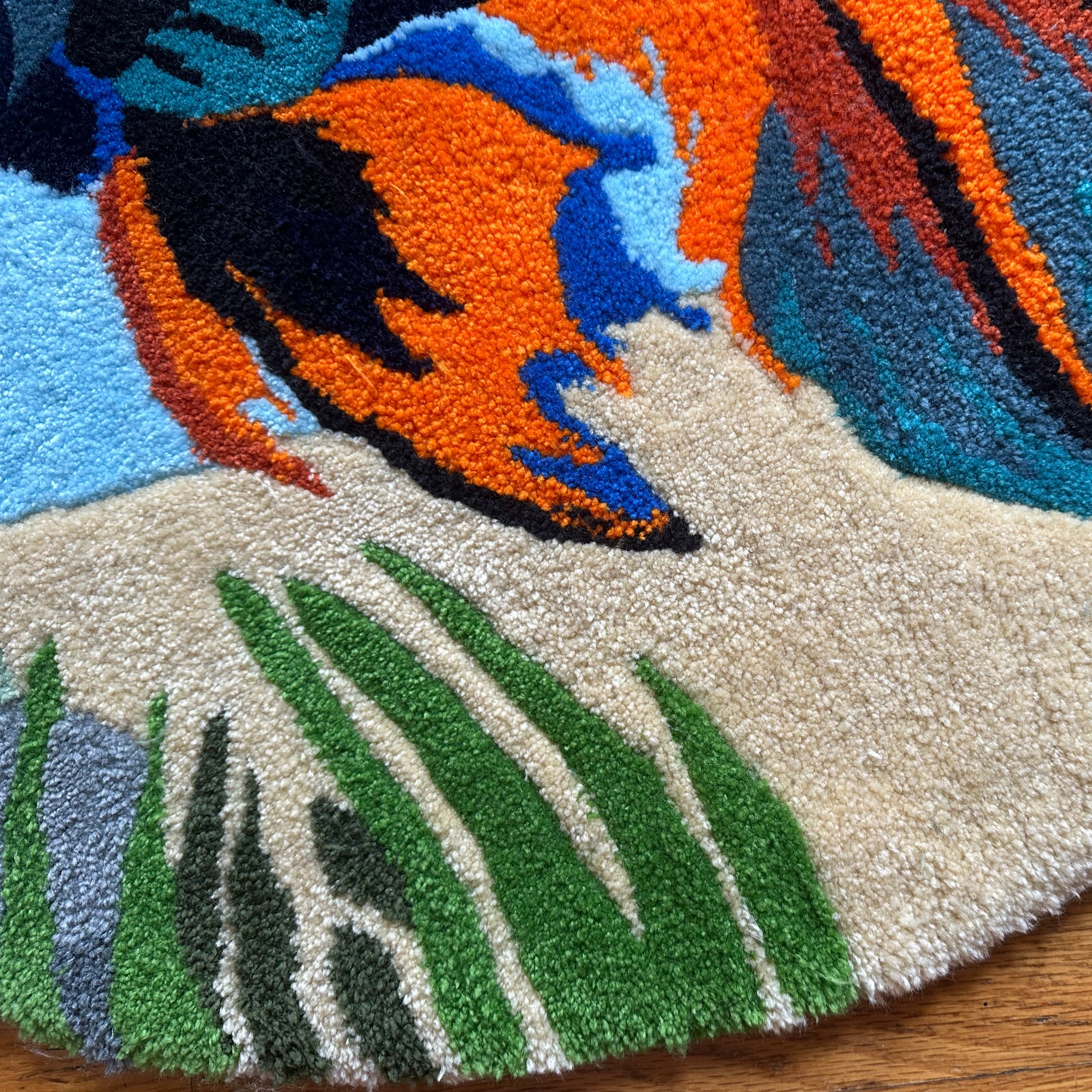 Close-up of colorful handmade betta fish rug showing detailed orange, blue, black, and green patterns on soft textured surface