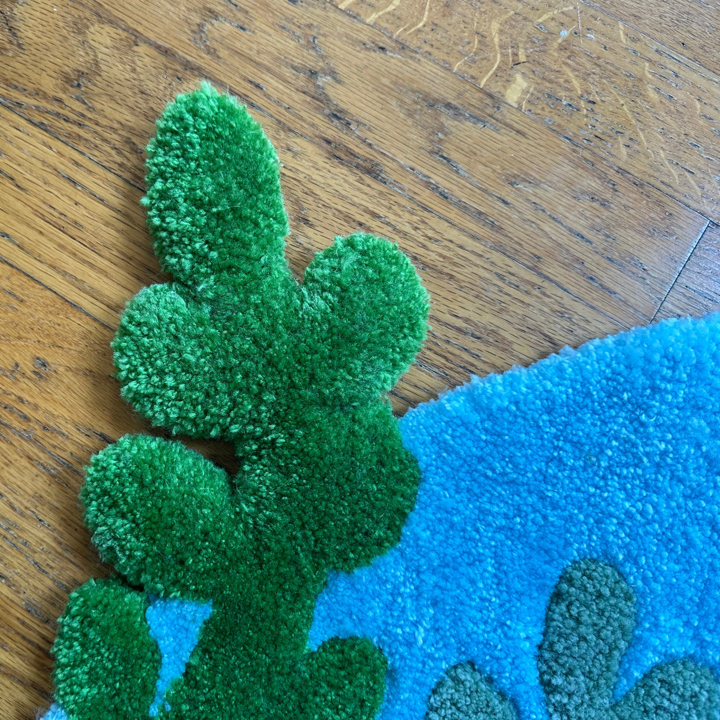 Close-up of handmade betta fish rug showing green textured leaf design and bright blue background