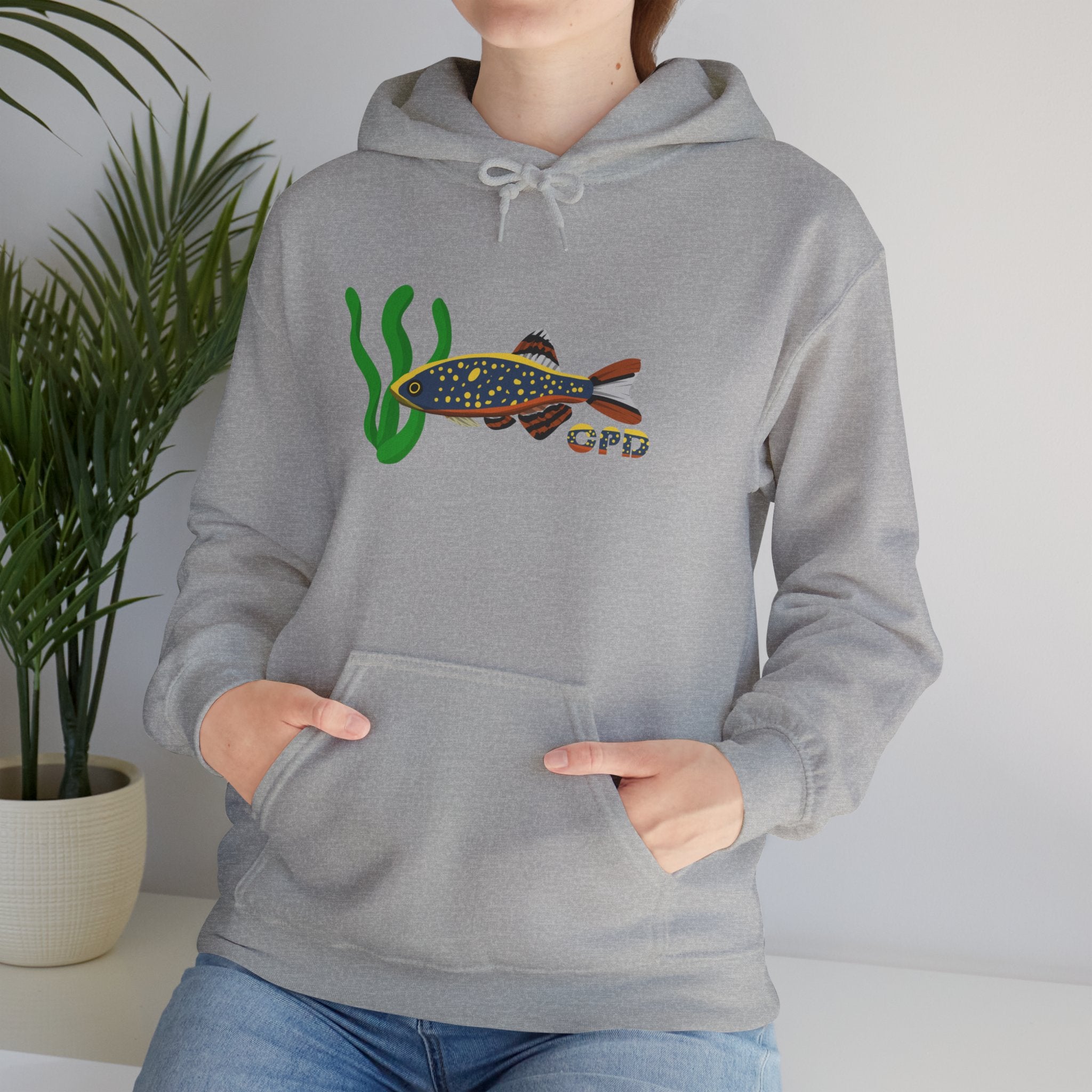 Woman sitting beside plant wearing grey hoodie with Celestial Pearl Danio fish graphic